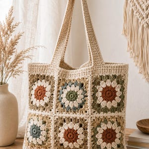 May include: A beige crochet tote bag with a floral pattern. The bag features a series of square panels, each with a flower design in shades of brown, green, and blue. The handles are a solid beige color.