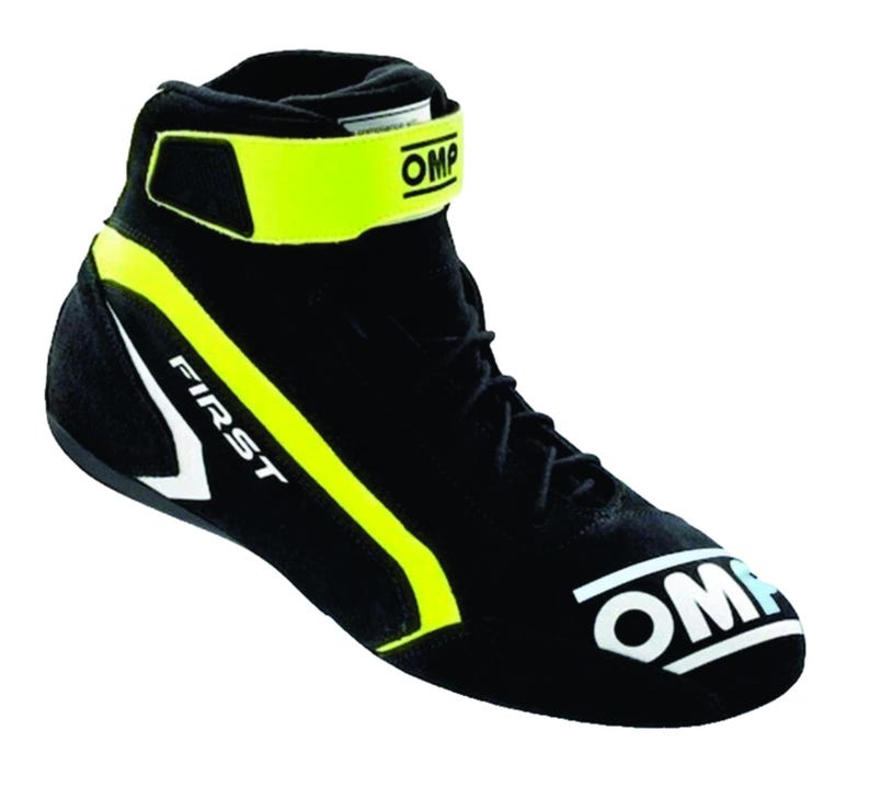 May include: A black high-top racing shoe featuring a bright yellow ankle strap with the OMP logo, black laces, and a white OMP logo on the toe. The side displays the word FIRST in white lettering with a yellow accent stripe along the heel area.