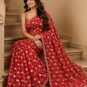 May include: A vibrant red saree featuring an intricate gold embroidered lattice pattern with circular floral motifs and small reflective mirror accents. The garment has a scalloped border with detailed gold stitching and a matching sleeveless blouse.