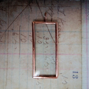 May include: A copper-toned metal frame with a clear glass insert. The frame has a loop at the top for hanging.