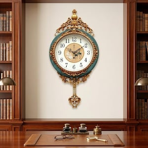 May include: A wall clock with a circular face featuring black Arabic numerals, a white background, and a central gold-toned graphic of two deer. The clock is encased in an ornate gold and teal frame with a decorative gold pendulum hanging below.