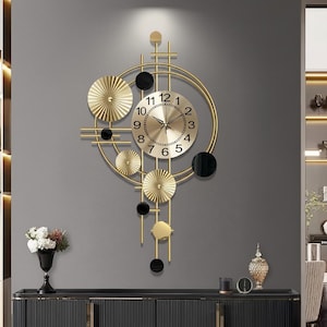 May include: Gold-toned wall clock with a modern design. The clock features a circular face with black numerals and hands, surrounded by a gold frame and decorative elements. The design includes gold circles and black accents, creating a stylish, contemporary look.