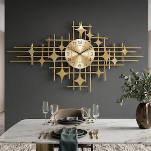 May include: A large gold-colored wall clock featuring a circular face with black numerals and hands, mounted on a geometric metal grid frame decorated with multiple four-pointed star shapes extending horizontally across the wall.