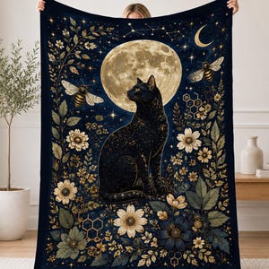 May include: A rectangular throw blanket featuring a dark blue background with a central black cat sitting before a large, full moon. The design includes golden bees, honeycomb patterns, white and blue flowers, green foliage, and a crescent moon.
