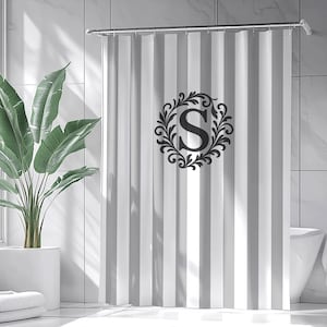 May include: A shower curtain featuring vertical white and light gray stripes with a centered dark gray monogram letter S enclosed within a decorative circular leafy vine frame. The curtain hangs from a silver rod with metal rings in a bathroom.