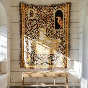 May include: A woven tapestry throw blanket featuring a tiger sitting inside a large decorative bowl. The design includes intricate floral patterns, a bird in a small archway, and a raptor in a larger archway, all in shades of gold, black, and brown.