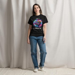 May include: Black t-shirt with a colorful brain graphic and the text "I.A.? I CREATE". The brain design features vibrant hues of blue, purple, yellow, and pink. The shirt is paired with blue jeans and white sneakers.