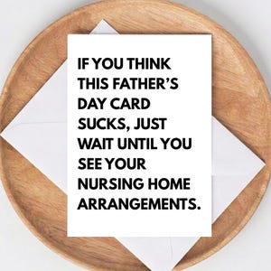 May include: A white Father's Day card with black text that reads: "IF YOU THINK THIS FATHER'S DAY CARD SUCKS, JUST WAIT UNTIL YOU SEE YOUR NURSING HOME ARRANGEMENTS." The card is inside a white envelope, resting on a wooden plate.