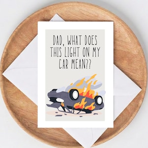May include: A greeting card with the text "DAD, WHAT DOES THIS LIGHT ON MY CAR MEAN??" features a cartoon of a burning car. The card is on a white envelope, placed on a wooden tray.