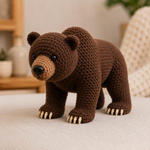 May include: A brown crochet bear toy featuring a dark brown body, a lighter brown muzzle, black plastic eyes, a black nose, and small cream-colored claws on each of its four paws. The bear is standing in a quadrupedal position with a textured yarn finish.