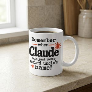 May include: A white ceramic mug featuring black text that reads "Remember when Claude was just your weird uncle's name?" with red horizontal lines and red starburst accents. The mug has a standard handle and a cylindrical body shape.