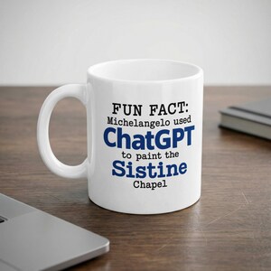 Puede incluir: Una taza de cerámica blanca con texto en negro y azul que dice: FUN FACT: Michelangelo used ChatGPT to paint the Sistine Chapel. La taza tiene un asa estándar y un acabado liso y brillante, presentando un diseño claro y legible.