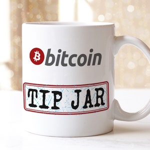 May include: White ceramic mug with a red Bitcoin logo and the text "bitcoin" in gray. Below the logo is a red and blue distressed rectangle with the text "TIP JAR" in black.