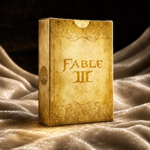 Op de afbeelding: Een rechthoekige doos met de tekst "Fable III" in gouden letters. De doos heeft een verouderde, perkamentachtige uitstraling met sierlijke gouden filigraan ontwerpen. Een cirkelvormig embleem staat op de zijkant van de doos. De achtergrond is een zachte, getextureerde stof.