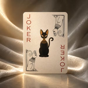 May include: A playing card featuring a black cat with gold accents, a stylized white cat, and the word "JOKER" in red. The card has an Egyptian theme and is set against a soft, textured background.