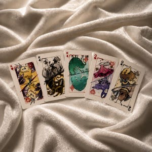 Handmade fantasy playing card set displayed on satin fabric with colorful illustrated face cards and artistic gaming deck aesthetic