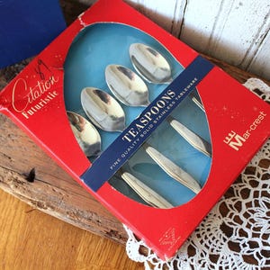 May include: A set of four silver-colored stainless steel teaspoons packaged in a red cardboard box with a blue window. The box features the text Citation Futuristic, TEASPOONS, FINE QUALITY SOLID STAINLESS TABLEWARE, and the Mar-crest logo.