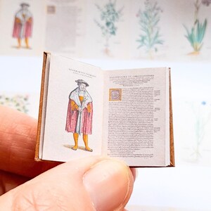 May include: A miniature book with a brown leather cover. The book is open to a page with an illustration of a man in a red and gold robe. The text on the page is in a black font.