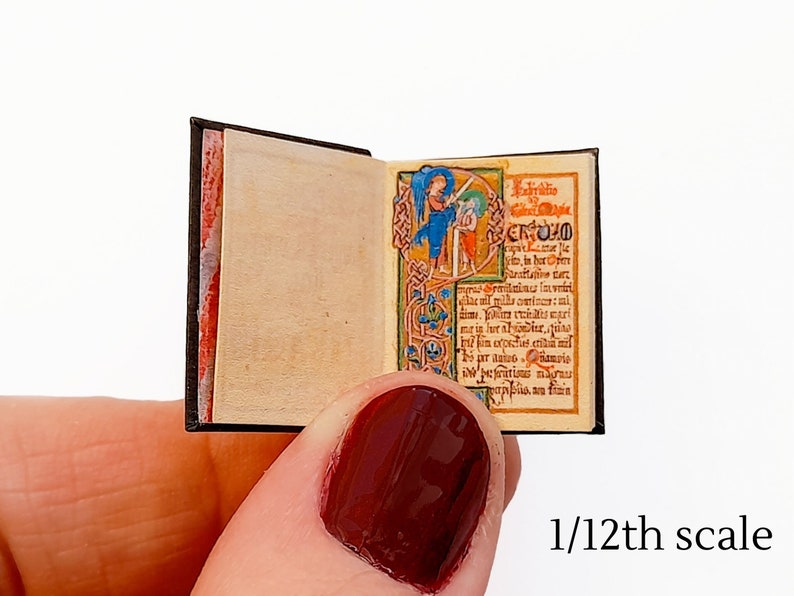 Pu&ograve; includere: Un libro in miniatura con una copertina nera e un'illustrazione dettagliata sulla pagina aperta. Il libro &egrave; in scala 1/12.