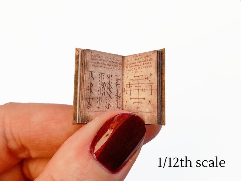 Pu&ograve; includere: Un libro in miniatura con una copertina in pelle marrone e dettagli dorati. Il libro &egrave; aperto su una pagina con testo scritto a mano e simboli. Il libro &egrave; in scala 1/12.