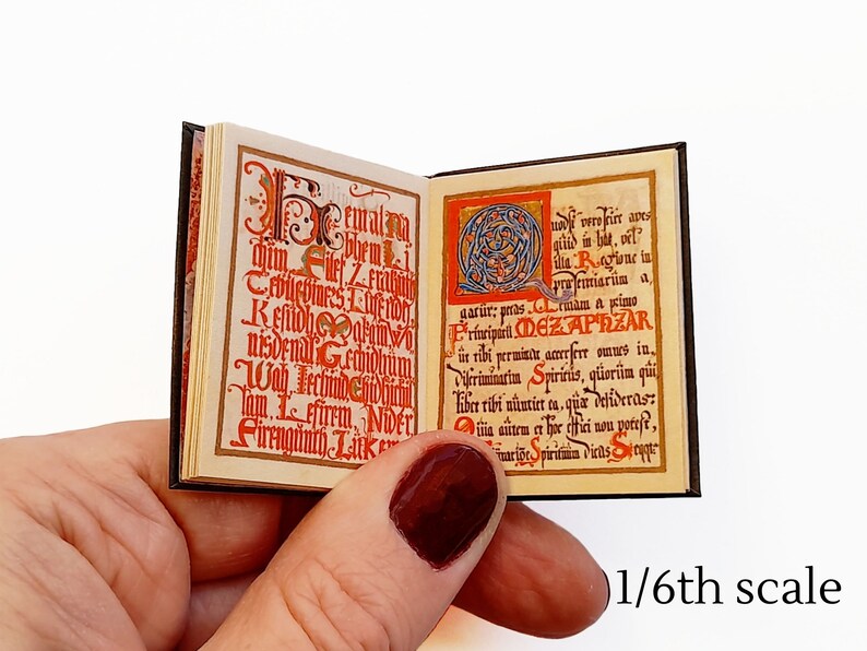Pu&ograve; includere: Un libro in miniatura con una copertina nera e lettere rosse e dorate. Il libro &egrave; aperto su una pagina con un'illustrazione rossa e dorata e testo in un carattere di stile medievale. Il testo dice "eturalim bhemi gar&uuml;r: pras ille Ragione in preemiari&uuml;n a rmam a kimo Kefidhearum Primiparil. DEZAPRZAR nisdenal Gechidhum ir ribi permintu amerfere omnes in. Vifiriminatin Spiriris, q&uuml;ori&icirc;m qui Wab echinochiiber rihi nuntiet ta, que defideras: Sirrnginth Luk lom Ffirem. NiDELi autem et her offici non poteft, unri&otilde;e Spirituia viens ot".