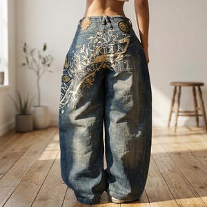 May include: Wide-leg blue denim jeans featuring a faded wash, a high-waisted fit, and intricate gold-toned embroidery across the back. The design includes decorative patches and detailed floral-inspired line art patterns on the rear pockets.