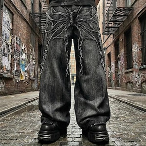 Könnte beinhalten: Schwarze Jeans mit weitem Bein und einem einzigartigen Spinnennetz-Design auf der Rückseite. Die Jeans haben eine verwaschene Optik und werden mit schwarzen Plateau-Stiefeln kombiniert. Das Bild ist in einer urbanen Gasse aufgenommen.