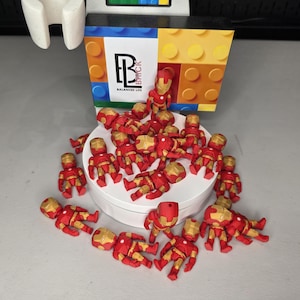 May include: A collection of small, red and gold Iron Man figurines are scattered on a white surface. A colorful box with the text "Balanced Life" and a logo is in the background. The figurines are in various poses.