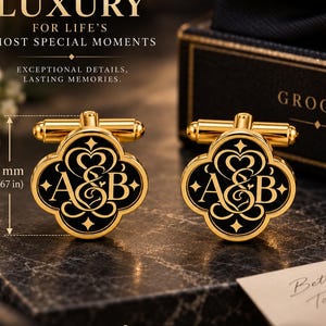 May include: A pair of gold-toned cufflinks with a black clover-shaped face featuring the letters A&B in a decorative script. The cufflinks measure 0.67 inches in height. The design includes ornate scrollwork and small star accents on the black surface.