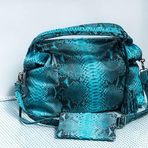 May include: A turquoise and black snakeskin-patterned handbag with a matching wallet. The handbag has a top handle, a shoulder strap, and a tassel. The wallet is rectangular and has a silver clasp.