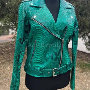 May include: A vibrant green leather jacket with a snakeskin pattern. The jacket features a classic biker style with a notched collar, asymmetrical zipper closure, and a belt at the waist. The text "Adt Reptile" is visible on the jacket.