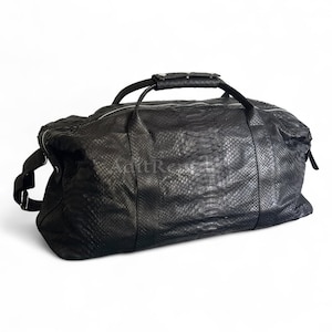 May include: Black duffel bag with a snakeskin texture. The bag has a top handle, two side handles, and a shoulder strap. The zipper runs along the top. The bag is made of a soft, flexible material.