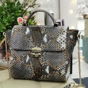 May include: A snakeskin-patterned handbag with a top handle and a gold-colored chain strap. The bag features a flap closure with a gold-colored clasp. The color palette includes shades of gray, brown, and white, creating a textured appearance.