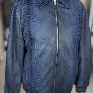 May include: A dark blue jacket featuring a textured snakeskin pattern throughout the entire garment. The jacket includes a standard collar, long sleeves, and a full-length silver-toned metal zipper closure down the center front.