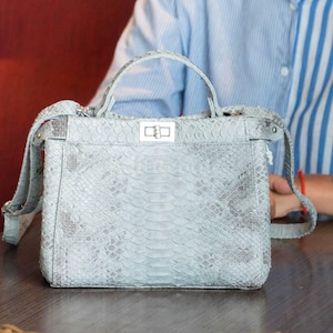 May include: A light blue handbag with a snakeskin pattern. The bag has a top handle and a detachable shoulder strap. It features a silver clasp closure and is made of a textured material.