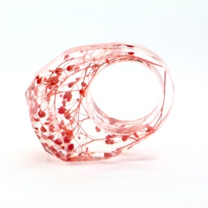 May include: A clear resin ring with a faceted design. The ring is embedded with delicate red floral elements, creating a unique and natural aesthetic. The ring's design is modern and eye-catching.