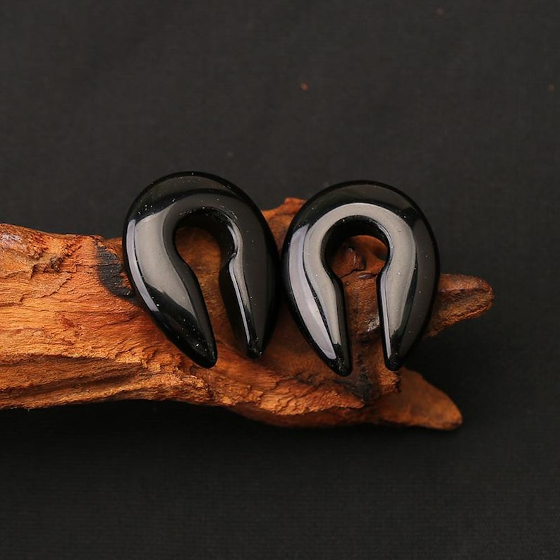 May include: A pair of black, horseshoe-shaped ear gauges with a smooth, polished finish. These U-shaped body jewelry pieces feature a solid, glossy surface and a curved design, crafted for ear stretching and body modification purposes.