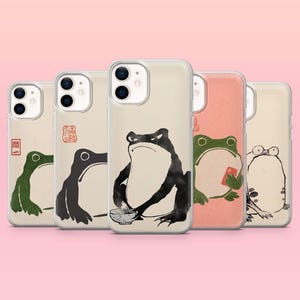 Peut inclure: Plusieurs coques de téléphone avec des illustrations de grenouilles dans un style artistique japonais. Chaque coque présente un design de grenouille différent en noir, vert et pêche, certaines tenant des objets. Les coques ont un design clair et protecteur.