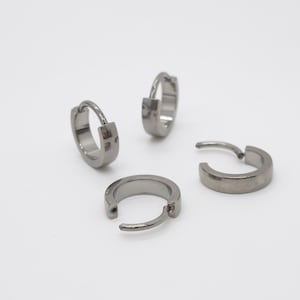 Peut inclure: Quatre petites boucles d'oreilles créoles circulaires en métal poli de couleur gris acier. Chaque boucle d'oreille est dotée d'un mécanisme de fermeture à charnière, permettant de l'ouvrir et de la fermer. La surface du métal est lisse et brillante.