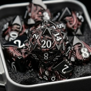 May include: A set of black and red polyhedral dice for tabletop games. The dice are in a metal container. The dice have white numbers and a detailed red design. The largest die shows the number 20.