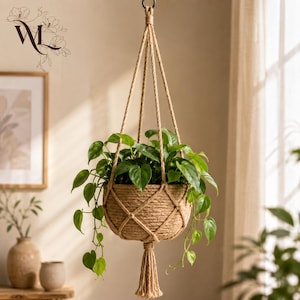 May include: A hanging plant holder made of thick, natural-colored jute rope with a woven net design. The holder contains a lush green pothos plant with heart-shaped leaves that spill over the sides. A decorative tassel hangs from the bottom.