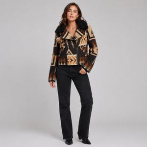 May include: A cropped moto-style jacket featuring a geometric pattern in shades of black, tan, and cream. The jacket has a black faux fur collar, long sleeves, and a front zipper closure, paired with solid black denim jeans and black pointed boots.