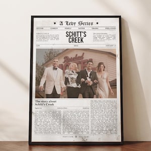 May include: A framed poster featuring a newspaper-style layout about the television show Schitt's Creek. The design includes the title, text columns, and a central photograph of four people standing in front of the Rosebud Motel building.