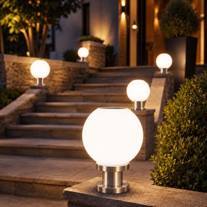 May include: A series of spherical outdoor post lights featuring glowing white glass globes mounted on brushed silver metal bases. These circular lamps are positioned along stone steps and ledges, providing illumination with a warm light output.