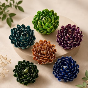 Puede incluir: Seis adornos florales decorativos en tonos verdes, turquesa, naranja, morado y azul. Cada flor tiene un acento dorado metálico. Las flores están dispuestas sobre una plataforma circular de color neutro.