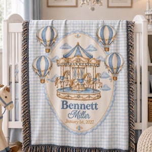 May include: A light blue and white gingham blanket featuring a central oval illustration of a carousel with horses, surrounded by four hot air balloons and clouds. The text Bennett Miller January 1st, 2027 is printed in blue, with fringed edges.
