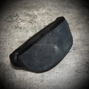 Pode incluir: Uma pochete preta e cinza com um padrão texturizado e pontilhado na frente. A bolsa tem um zíper preto e um design elegante e moderno. A bolsa é feita de um material durável.