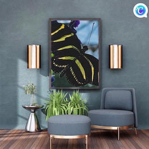 May include: A framed butterfly art print with a black and yellow striped pattern hangs above a blue chair and ottoman. The room features a silver side table with a plant, two wall sconces, and a wooden floor.