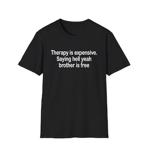 Puede incluir: Una camiseta negra de manga corta con texto blanco impreso en el pecho que dice: Therapy is expensive. Saying hell yeah brother is free. La prenda tiene un cuello redondo estándar y un dobladillo recto sobre un fondo liso.