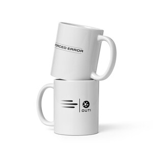 May include: Two white ceramic mugs stacked on top of each other. The top mug has the text "FORCED ERROR" printed in black. The bottom mug features a soccer ball graphic with the word "OUT!" printed below it.
